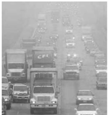 Imagen de tráfico denso en una autopista con camiones y coches bajo un ambiente brumoso.