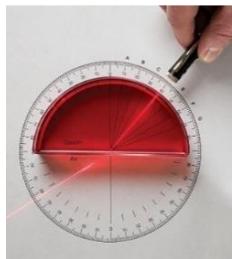 Fotografía de un experimento de óptica con un haz láser atravesando un bloque semicircular sobre un transportador de ángulos.